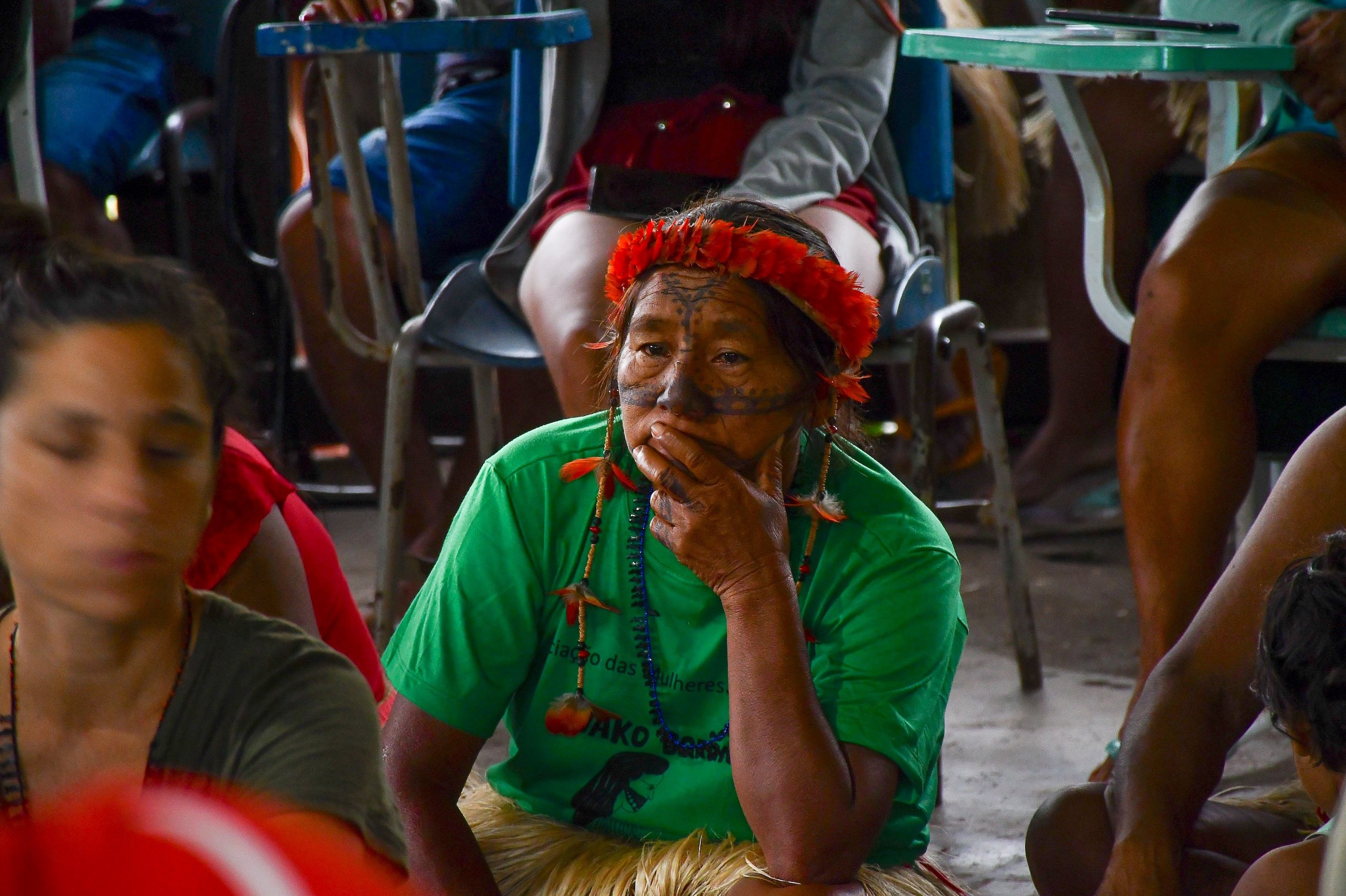 Una mujer indígena con una blusa verde y adornada con decoraciones coloridas sentada en medio de una reunión